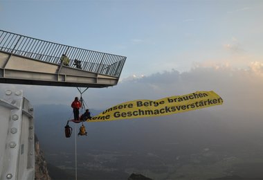 Freischwebend in einem Höhenbiwak mit Banner „Unsere Berge brauchen keine Geschmacksverstärker“.